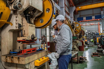 Industrial engineers wearing safety gear inspecting heavy machinery in a modern factory. Factory...