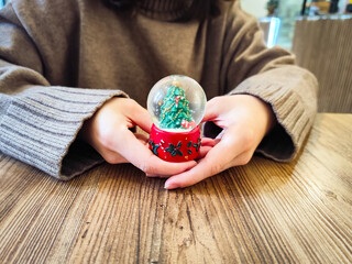 Small christmas snow globe with Chirstmas tree, Hands gently holding a small snow globe