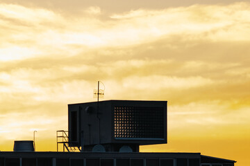 HVAC unit on building rooftop, silhouetted against a golden cloudy sky at sunset. Industrial...