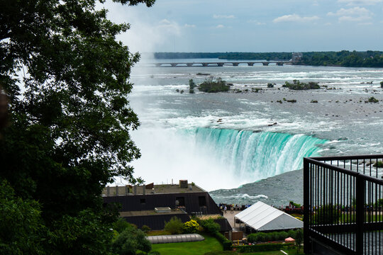 View of the powerful turquoise waters plunging over the cliffside into the misty depths below, framed by lush greenery, Niagara Falls, Ontario, Canada.