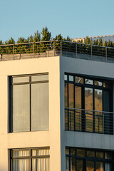 Architecture building with large glass windows and a rooftop garden under clear sky, showcasing...