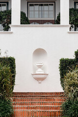 Classic white stucco facade with red brick stairs and lush green bushes, timeless architecture and...