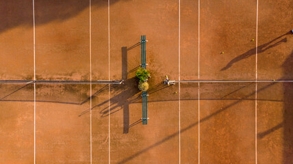 Aerial view of the clay tennis court with its crisp white lines, bisected by a dark net and bench casting long shadows, Sint Maarten, North Holland, Netherlands.