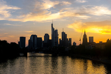 View of a dramatic skyline silhouette against a sunset sky with golden light reflecting on the river below, Frankfurt am Main, Hessen, Germany.