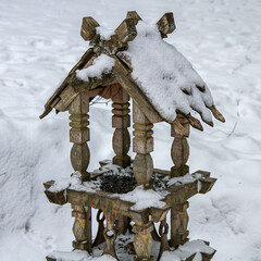 A simple wooden bird feeder, placed outdoors and covered in fresh winter snow. A seasonal nature...