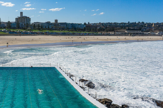View of the vibrant turquoise pool contrasting with the frothy white waves crashing against the rocks, a serene beach scene unfolds, Bondi Beach, New South Wales, Australia.