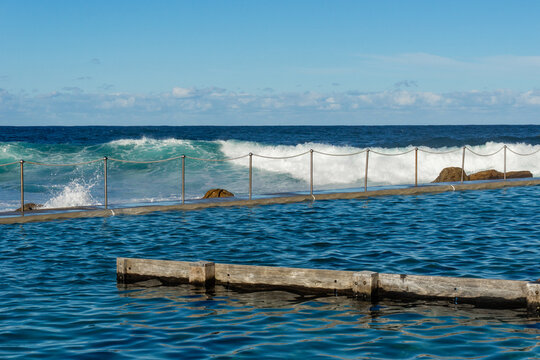 View of the ocean's raw power as waves crash against the protective barrier of Bronte Baths, a serene contrast of blue hues, Bronte, New South Wales, Australia.