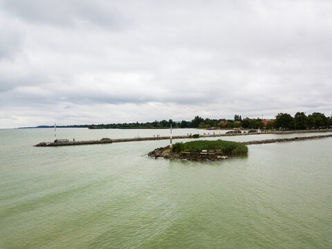 Aerial view of the Fony&oacute;di m&oacute;l&oacute; stretching into the lake under a cloudy sky, its light contrasting with the muted greens of the water, Fonyod, Hungary.