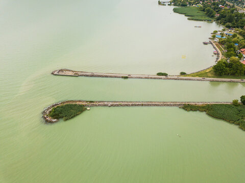 Aerial view of the Fony&oacute;di m&oacute;l&oacute; jetties stretch into the tranquil green waters, a stark contrast to the lush vegetation along the shore, Fonyod, Hungary.