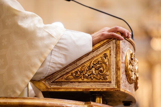 Priest's hand resting on ornate church pulpit during ceremony