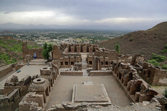 View of ancient ruins stand weathered against a backdrop of misty mountains and a sprawling valley under a somber sky, Takht Bhai, Khyber Pakhtunkhwa, Pakistan.