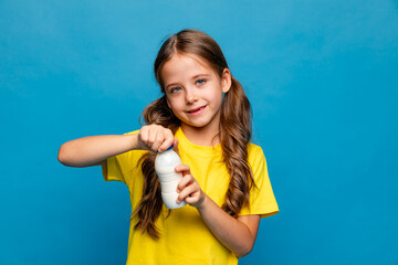 Cute little brunette girl in a yellow t-shirt holding a bottle with fresh tasty yogurt on light...