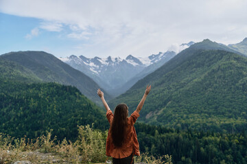 Nature lovers embrace a dramatic mountain landscape as a lone hiker raises hands in triumph at a sweeping valley overlook, with distant snow capped peaks and clear blue skies.