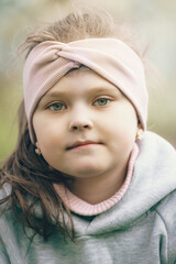 A Portrait of a Young Girl Wearing a Soft Pink Headband with Gentle Expressions, Showcasing Facial Features and a Natural, Outdoor Setting