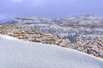 View of snow-dusted, rust-colored rock formations cutting jagged lines against the muted sky, creating a stark contrast, Bryce Canyon, Utah, United States.