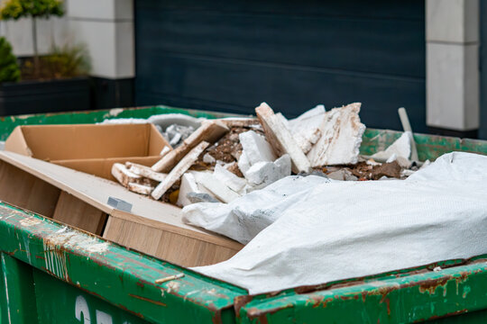 Construction waste container filled with rubble insulation boards and renovation debris placed in front of a modern residential building