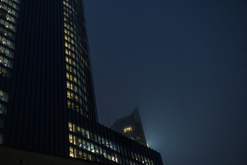 Modern office buildings with glowing windows in a foggy night city. cinematic night shot of sleek glass office towers in a metropolitan business district. Warm lights from the windows contrast