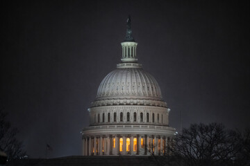 View of the United States Capitol Building glows warmly against a dark, overcast sky, highlighting its iconic dome and intricate architecture, Washington DC, Washington DC, United States.