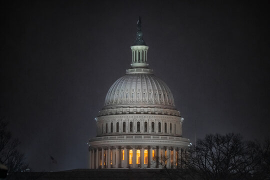 View of the United States Capitol Building glows warmly against a dark, overcast sky, highlighting its iconic dome and intricate architecture, Washington DC, Washington DC, United States.