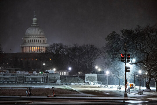 View of the United States Capitol Building illuminated against the dark sky during a snowstorm, contrasting with the quiet streets, Washington DC, Washington DC, United States.