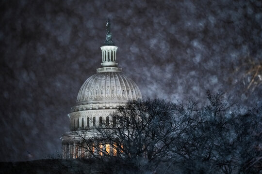View of the United States Capitol Building stands as a beacon through a flurry of snow, its dome illuminated against the dark sky, Washington DC, Washington DC, United States.