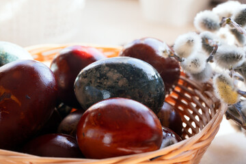 Close-up of shiny naturally dyed Easter eggs in wicker basket with pussy willows