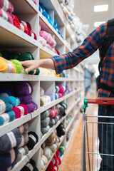 Man choosing yarn from colorful craft store shelves