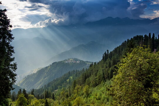 View of sunbeams piercing dramatic clouds over forested mountains, casting ethereal light across the rugged landscape, Sri Paye, Khyber Pakhtunkhwa, Pakistan.