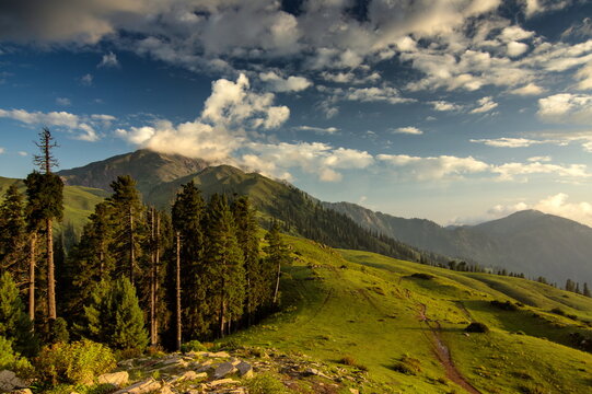 View of lush green hills meeting the majestic mountains under a sky painted with clouds, Sri Paye, Khyber Pakhtunkhwa, Pakistan.