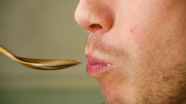 Profile close up young unshaven man mouth eating traditional olivier salad, also known as potato salad, bringing golden spoon to his lips, chewing food contentedly. Man eating olivier