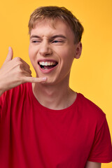 Smiling man in a red shirt makes a shaka gesture against a vibrant yellow background, expressing fun, positivity, and friendly communication in a candid studio shot, ideal for branding