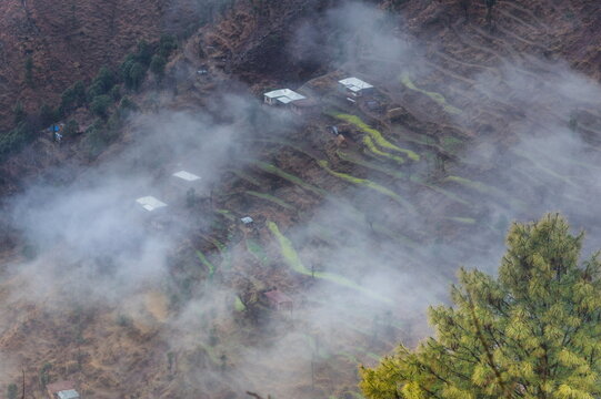 View of houses dotted across terraced slopes shrouded in ethereal mist, creating a serene landscape of contrasting textures and tones, Muzaffarabad, Azad Kashmir, Pakistan.
