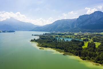 Aerial view of Mondsee lake glistening emerald green against the backdrop of verdant forests and the majestic Schafberg mountain, Mondsee, Upper Austria, Austria.