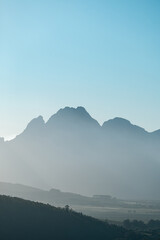 Misty mountain range under clear blue sky with soft light at sunrise