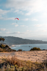 Paraglider flying above coastal landscape with ocean in background © Braeden