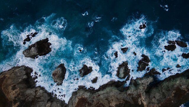 Aerial view of ocean waves crashing against rocky coastline - Powered by Adobe