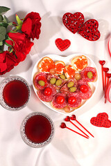 Heart of fresh canapes with salami, caviar, cheese and grapes for a buffet with roses, red wine and red hearts on the festive table. Valentine's Day dishes, advertising banner, bar invitations, menu.