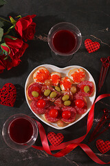 Valentine's Day food, heart of fresh canapes with salami, caviar, cheese and grapes for a buffet with roses, red wine, red hearts for the festive table, banner for advertising or invitation at the bar