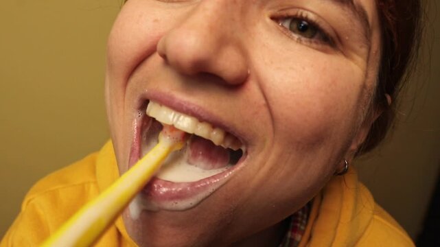 Close-up of woman in yellow shirt brushing teeth with yellow toothbrush, foam visible. Daily oral hygiene routine