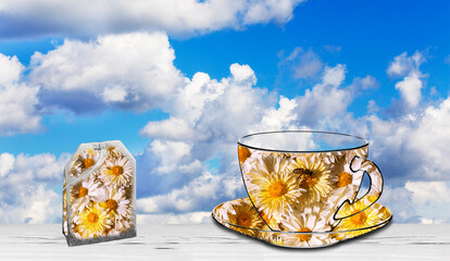 Against the background of a blue sky, chamomile flowers in the shape of a cup and saucer and a chamomile tea bag.