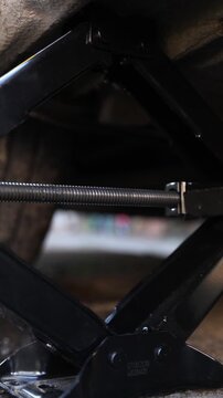 Vertical video. Jack screw lowers and raises car body before carrying out complex repair process. Special threaded tool shaped jack provides smooth movement of flat vehicle underbody and positioning