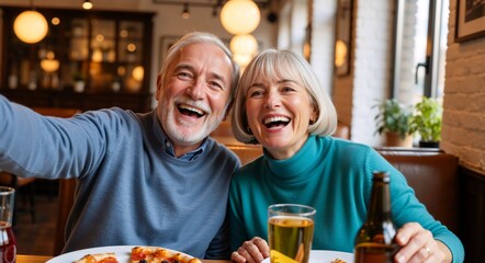 Cheerful senior couple taking a selfie while dining in a pub. Happy retired man and woman laughing together over pizza and beer
