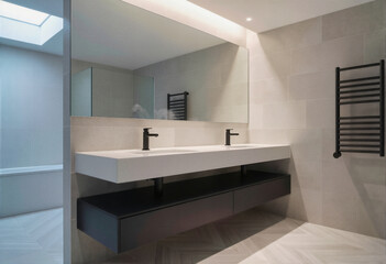 Fototapeta premium Modern bathroom with white double vanity, black fixtures, large mirror, and herringbone tile floor.