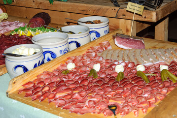 Traditional Alpine charcuterie platter with sliced cured meats, speck, bread, cheese, and pickles on a rustic wooden board, showcasing regional cuisine and gourmet food.