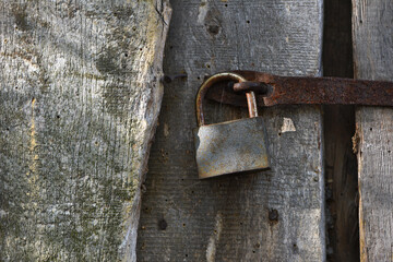 old padlock. Closeup view of an old padlock covered in rust, attached to a cracked wooden door. It represents themes of security, the passage of time, decay, and vintage aesthetics. the door is locked
