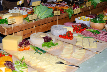 Rustic gourmet cheese and charcuterie buffet with assorted cheeses, cured meats, cherry tomatoes and fresh vegetables on wooden boards for catering and food events.