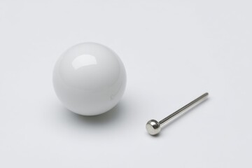 White ball next to a metal pin on a plain background, showcasing a minimalist design and simple objects in a controlled setting in natural light