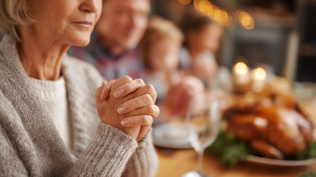 Close up of faceless multigeneration family holding hands while praying heavily defocused Thanksgiving dining table background anonymous group with spiritual tradition holiday