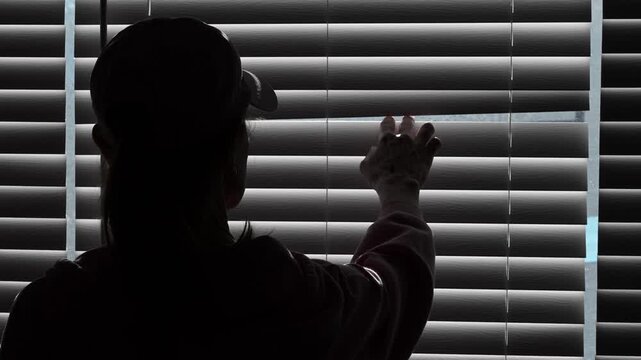 Woman looking through blinds in dark.