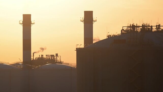 Sunset view of industrial structures with smokestacks against the sky in an urban area
